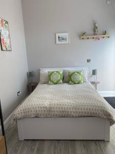 a white bedroom with a bed with green pillows at Hugo Mews Bright Studio Apartment in Bray