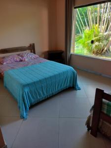 a bedroom with a bed with a blue blanket and a window at Canto Caiçara Hostel in Paraty
