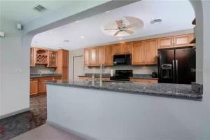a kitchen with wooden cabinets and a black refrigerator at Canal Front 3-Bedroom Grand Villa with Pool in Port Charlotte