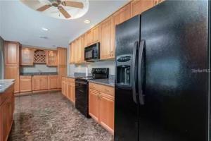 a kitchen with a black refrigerator and wooden cabinets at Canal Front 3-Bedroom Grand Villa with Pool in Port Charlotte