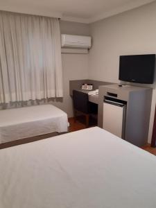 a room with two beds and a desk with a television at Biazi Plaza Hotel in Bauru