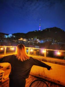 a woman standing on a ledge looking at a city at night at Namsan Guesthouse in Seoul