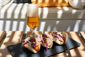 two appetizers on a black plate with a glass of beer at Kouros Village Hotel - Adults Only in Perissa