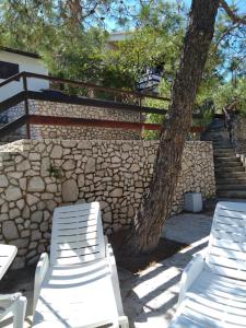 two white chairs and a tree next to a stone wall at Holiday home Marina in Sali