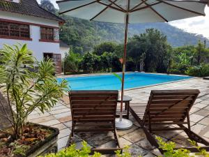 duas cadeiras e um guarda-sol junto a uma piscina em Agellum Bed & Breakfast em Domingos Martins