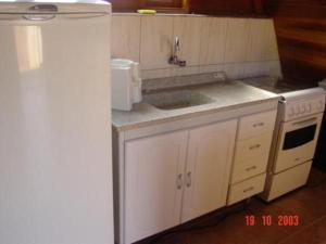 eine Küche mit weißen Schränken, einer Spüle und einem Kühlschrank in der Unterkunft Chalès em Ilhabela Litoral Norte in Ilhabela