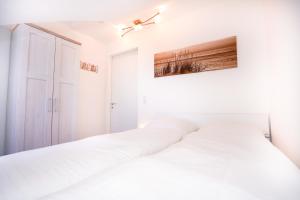 2 weiße Betten in einem weißen Schlafzimmer mit Deckenventilator in der Unterkunft Haus Atlantic Whg "Ferijentied" in Grömitz