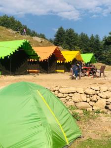 City Escape Camps and Cafe Kheerganga في Kheerganga: خيمة خضراء على الأرض مع أشخاص يجلسون على الطاولات