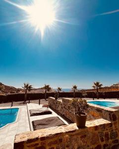 a view of two swimming pools with the sun in the sky at Aurora Mykonos Villas in Kalafatis