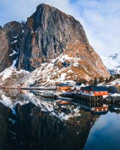 a mountain with a reflection in the water with houses at Reinefjorden Sjøhus in Reine