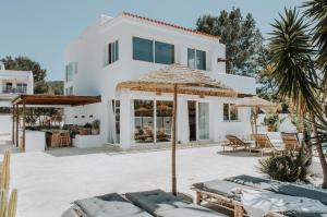 ein weißes Haus mit einer Terrasse mit Stühlen und Sonnenschirmen in der Unterkunft Casa Stellar - boutique villa with private heated pool and sea view - sustainably solar powered in San Jose de sa Talaia