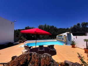 uma piscina com um guarda-sol vermelho e cadeiras em Silves Country Room em Silves