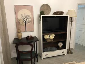TV in un armadietto bianco con sedia e tavolo di Il Fiore Bianco a Capo dʼOrlando
