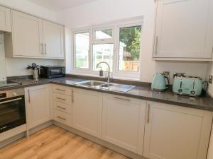 a kitchen with white cabinets and a sink and a window at Treestumps in Benllech