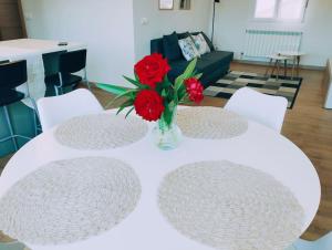 une table blanche avec des fleurs rouges dans un vase sur elle dans l'établissement Precioso apartamento en Pamplona junto al centro, à Pampelune