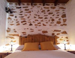 1 dormitorio con pared de piedra, 1 cama y 2 lámparas en Casa antigua en el centro de Fuerteventura, en Antigua