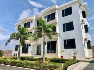 a white building with palm trees in front of it at APARTAMENTO PUERTO MADERA in Manta