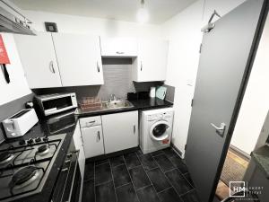 una pequeña cocina con armarios blancos, lavadora y secadora. en Enfield House - Beautiful 2 Bed - Good Transport Free Parking en Enfield Lock