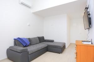 ein Wohnzimmer mit einem grauen Sofa und einem TV in der Unterkunft Apartments by the sea Duce, Omis - 4795 in Dugi Rat