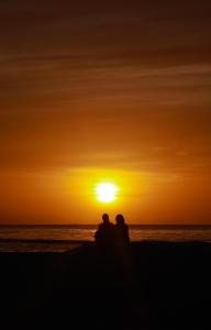 Una coppia seduta sulla spiaggia a guardare il tramonto di Cowry Inn a Fulidhoo
