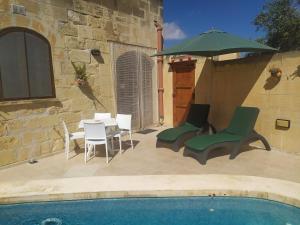 a patio with a table and chairs and an umbrella at Gozo Rustic Farmhouse with stunning views and swimming pool in Sannat