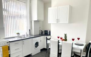 a kitchen with white cabinets and a table with wine glasses at Cosy Cheerful 2 Beds Near Piccadilly, Etihad Stadium Sleeps upto 5 in Manchester