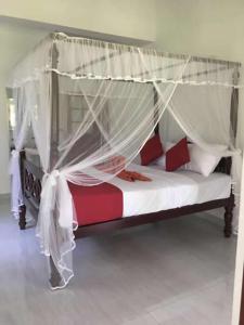 ein Schlafzimmer mit einem Himmelbett mit weißen und roten Kissen in der Unterkunft Lush Green Villa in Talpe