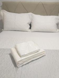 ein Stapel Handtücher auf einem weißen Bett mit Kissen in der Unterkunft Casa 2 Encanto dos Mares in Itapema