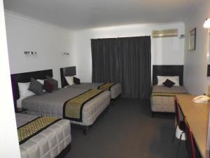 a hotel room with two beds and a desk at Burke & Wills Motor Inn in Kingaroy