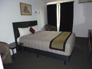 a bedroom with a bed, chair, and nightstand at Burke & Wills Motor Inn in Kingaroy
