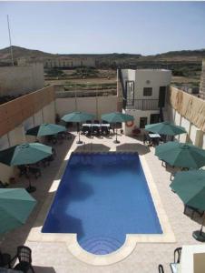 una gran piscina con sombrillas, mesas y sillas en Qronfli Holiday Apartments With Swimming Pool, en San Lawrenz