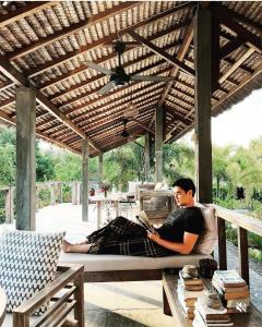 un uomo seduto su un letto sotto un pergolato con un libro di Manusia Dunia Green Lodge a Gili Air