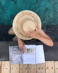 a woman with a hat and a magazine next to a pool at Manusia Dunia Green Lodge in Gili Islands