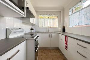 a small kitchen with white cabinets and a sink at Braemar 9 in Forster
