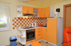 a small kitchen with orange cabinets and a refrigerator at Apartment Njivice 5295b in Njivice