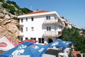 a white building with blue umbrellas in front of it at Apartments and rooms with parking space Stara Baska, Krk - 5447 in Stara Baška