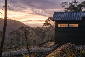 a cabin in the woods with the sunset in the background at Tiny Escapes Cradle Valley in Moina