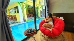 a woman sitting in a red chair next to a pool at PHỐ CHỢ ĐÊM Villa in Hoi An