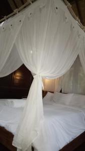 a white canopy bed with white curtains on it at Mulia Home Stay in Nusa Dua