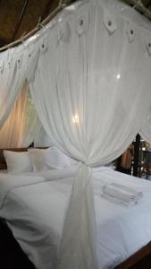 a white canopy bed with white sheets and pillows at Mulia Home Stay in Nusa Dua