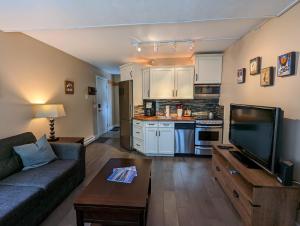 a living room with a couch and a tv and a kitchen at Steps to All New Gondola, Sleeps 4 with Free Parking in Whistler