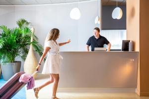 a woman pulling luggage in an office with a man behind a counter at ibis Styles Toulon Centre Port in Toulon