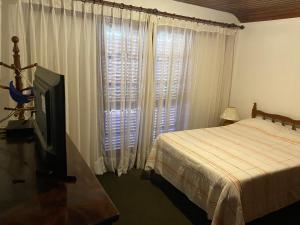 Casa encantadora na serra-Teresópolis في تيريسوبوليس: غرفة نوم بسرير وتلفزيون بشاشة مسطحة