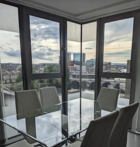 einen Glastisch und Stühle in einem Zimmer mit Fenstern in der Unterkunft Glasgow City Centre Waterfront Apartment in Glasgow