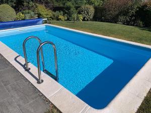 a blue swimming pool with two metal rails in a yard at Maudon Coeur de Baie in Ponts