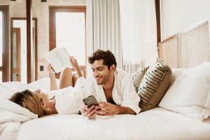un hombre y una mujer acostados en una cama mirando un celular en CIGNO HOTEL BOUTIQUE- Adults Only en Mérida