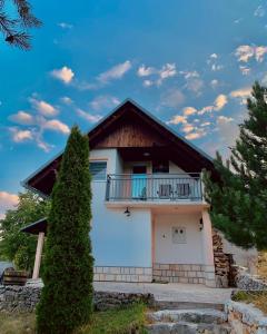 een wit huis met een balkon en een boom bij Planinska kuća za odmor Perić in Prozor