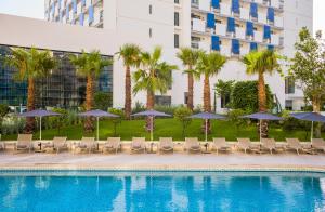 a pool with chairs and umbrellas and palm trees at Barceló Tanger in Tangier