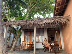 a woman sitting in a chair under a straw roof at La-Vira Beach Villa in Hikkaduwa
