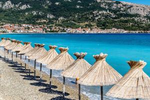 a row of straw umbrellas on a beach at Apartments with a parking space Baska, Krk - 5411 in Baška